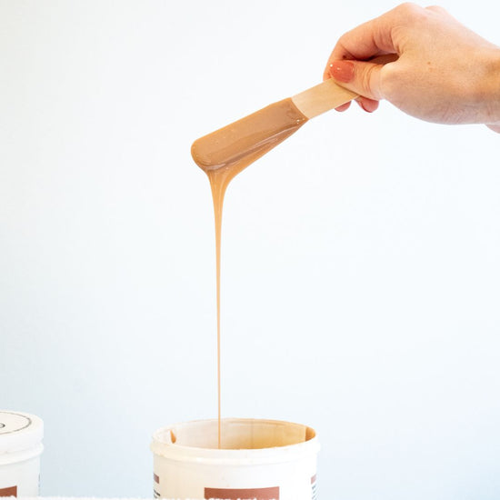 Wax stick being held over a waxing pot with waxing dripping down 